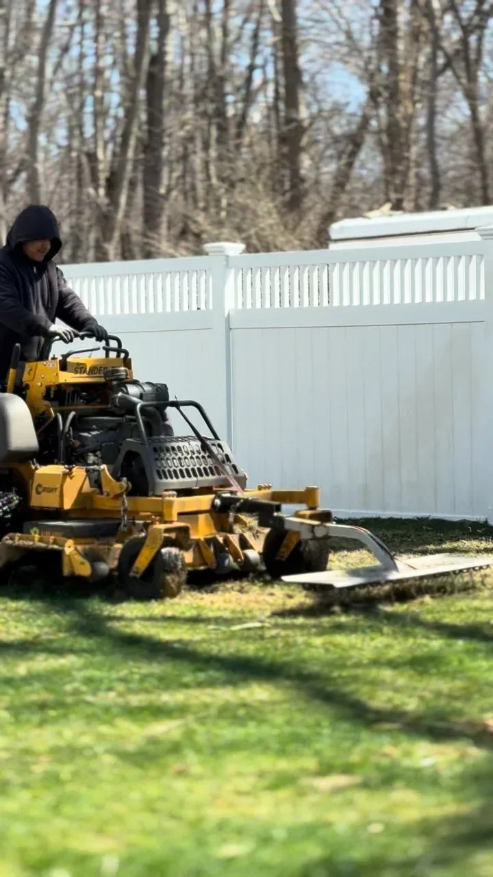 Crew member operating a stand-on mower along a vinyl fence line